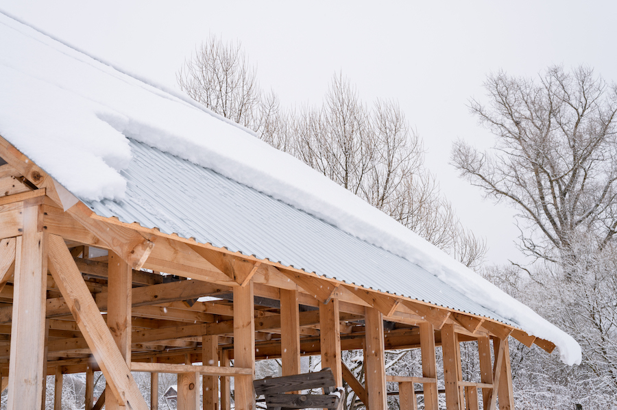 snow sliding down from roof. building construction house with metal roof covered fresh icy frozen snow 