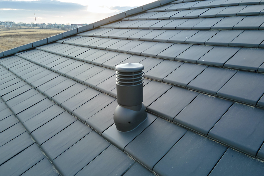 Closeup of ventilation pipe on house roof top covered with ceramic shingles. Tiled covering of building.